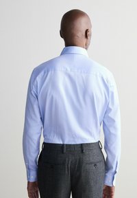 Hellblaues Hemd mit Knopfleiste und strukturiertem Muster, mit klassischem Kragen, langen Ärmeln und weißen Knöpfen, kombiniert mit grau strukturierten Hosen.