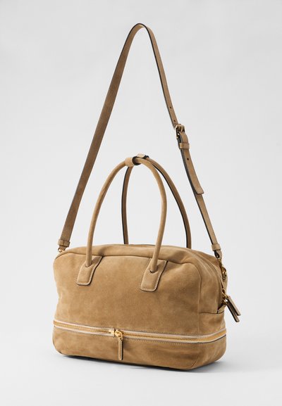 Torebka wykonana z tanowego zamszu, z dwoma górnymi uchwytami oraz regulowanym paskiem na ramię. Posiada złoty zamek błyskawiczny i gładką teksturę.