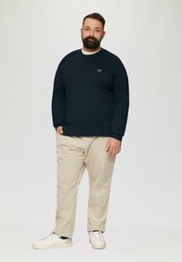 Marineblauwe trui met ronde hals, textuurstof en klein logo op de borst; gecombineerd met lichtbeige corduroy broeken en witte sneakers.