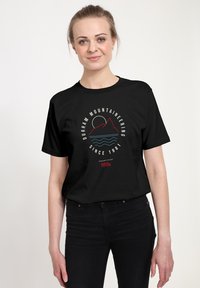 Sort kortærmet t-shirt med en cirkulær grafik med bjerge, en sol og teksten "Durham Mountaineering Since 1981" i hvid og rød.