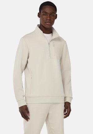 Beige half-zip sweatshirt van zacht materiaal met een voorzak, zijzakken met rits en geribde manchetten, gecombineerd met bijpassende broek.