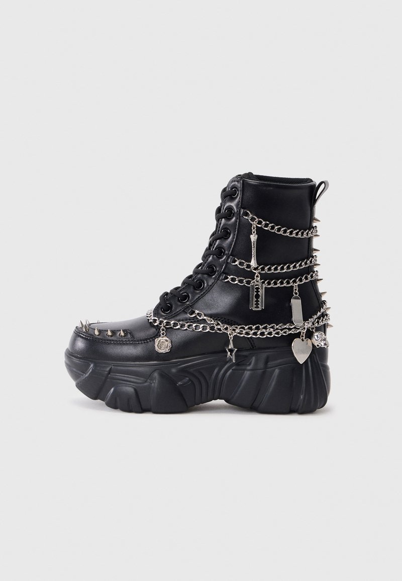 Melnas potītes zābaki, izgatavoti no sintētiskā materiāla, ar masīvu platformu, rotāti ar sudraba ķēdēm, tapām un metāla piekariņiem dekorācijai.