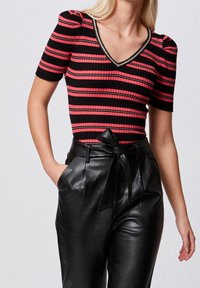 Haut côtelé à rayures rouges et noires avec manches courtes et col en V, orné d'un col souligné d'accent métallique. Associé à un pantalon en cuir noir taille haute.