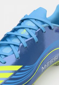 Blue soccer cleat with glossy finish, featuring blue laces, a yellow accent stripe, and "MESSI" branding on the side.