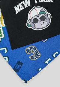 Maglietta nera con testo bianco "NEW YORK" e grafica di una scimmia in stile cartone animato, sovrapposta a un tessuto blu con varie stampe e numeri a tema sportivo.