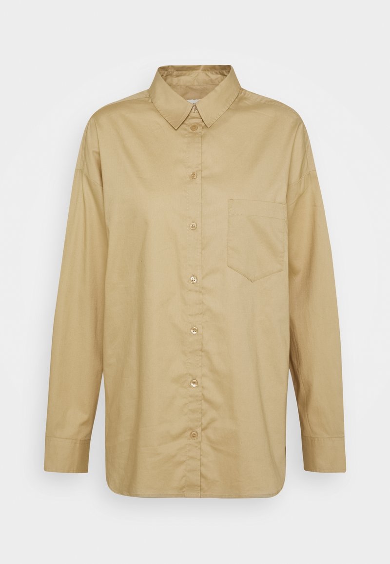 Chemise beige à manches longues avec boutons, col et une poche poitrine unique, présentée sur un fond clair uni.