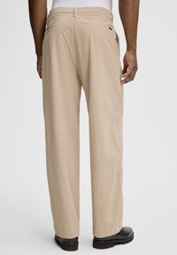 Beżowe spodnie sztruksowe z pionowym prążkowaniem, elastyczną talią, dwoma tylnymi kieszeniami i prostym krojem nogawek. Obuwie czarne z teksturowaną podeszwą.