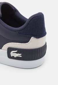 Zapatillas de piel azul marino con talón acanalado texturizado, acento de ante, suela de goma y logo embosado en el lateral. Presenta un diseño simple y deportivo.