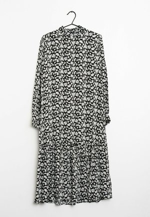 Musta kukkamekko pitkähihaisilla, jossa on valkoisia kukkia, korkea kaula-aukko ja kerroksellinen helma, joka luo virtaavan siluetin. Valmistettu kevyestä kankaasta.