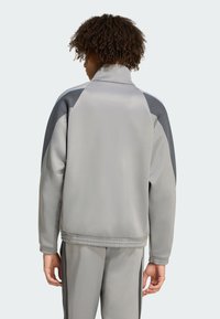Sivý športový sak s vysokým golierom, s kontrastnými tmavosivými akcentmi na pleciach a po stranách, hladká textúra a elastický pás.