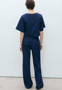 Temno modra kratka majica s širokimi rokavi, v kombinaciji z ohlapnimi hlačami, izdelanimi iz teksturiranega blaga.