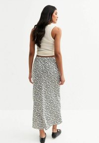 Maxi-jurk met een zwart-wit stippenpatroon. Materiaal lijkt zacht met een vloeiende uitstraling. Gestyled met een aangesloten crème tanktop.