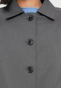 Κοντινή λήψη σε γκρι παλτό με κουμπιά στο γιακά και το πάνω μέρος του στήθους, με μια ματιά σε ανοιχτό μπλε ριμπ μπλουζάκι από μέσα.