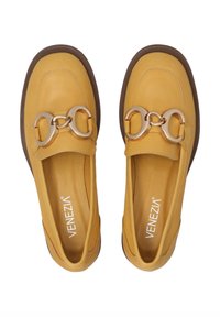 Żółte skórzane loafersy z dużym złotym łańcuchem z przodu, posiadające brązową gumową podeszwę oraz gładki, minimalistyczny design.