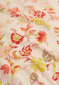 Tissu floral avec un fond beige clair, orné de motifs de fleurs rouges, roses et feuilles vertes vibrantes, présentant une texture lisse.