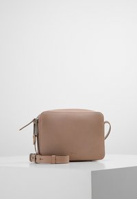 Borsa a tracolla in pelle marrone con forma rettangolare, chiusura con zip e tracolla regolabile. Texture liscia con un sottile dettaglio di branding.