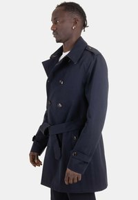 Trench coat blu navy con bottoni doppi, cintura in vita e spalline sulle spalle. Tessuto liscio e vestibilità su misura.