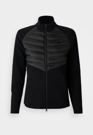 Schwarze Zip-Jacke mit gepolstertem Brustpaneel, gerippten langen Ärmeln und hohem Kragen, mit einem kleinen gestickten Logo auf der Brust.
