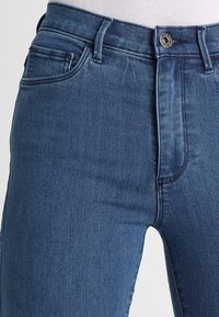 Jeans in denim blu scuro con un design aderente, stile classico a cinque tasche, chiusura con bottone e lieve scolorimento sulle cosce per effetto texture.