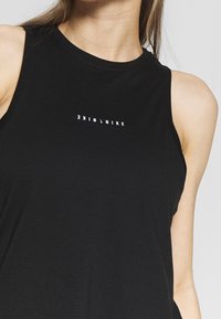 Czarny bezrękawnik sportowy wykonany z gładkiego materiału, z okrągłym dekoltem i subtelnym białym logo "NIKE" na piersi.