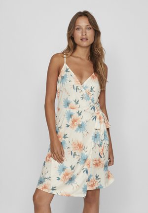 Bloemen wikkeljurk met spaghetti bandjes, met een crèmekleurige achtergrond, perzik- en blauwe bloemenprint, en een strikdetail bij de taille.