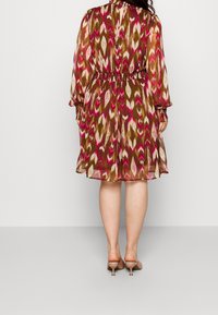 Šaty s ikatovým vzorem v hnědé, růžové a krémové barvě; dlouhé rukávy, zúžený pas, délka ke kolenům, lehká tkanina a knoflíkové detaily na zadní straně.