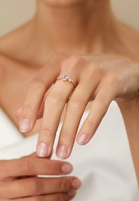 Goldring mit einem zentralen ovalen rosafarbenen Edelstein und zwei kleinen weißen Steinen auf jeder Seite. Glatter Ringkörper mit polierter Oberfläche.