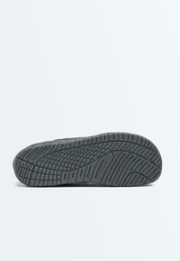 Semelle de chaussure en caoutchouc noir avec des motifs texturés antidérapants et le nom de la marque "OSHKSO" embossé près de la zone de la voûte plantaire.