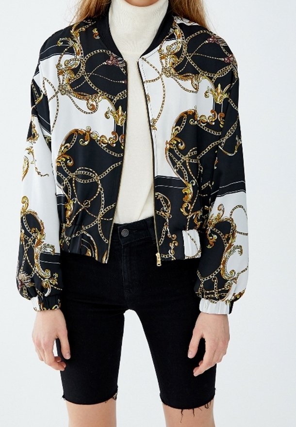 Veste bomber avec un motif noir et blanc orné de chaînes dorées. Fabriquée en matériau lisse, elle possède une fermeture éclair à l'avant et des poignets élastiques.