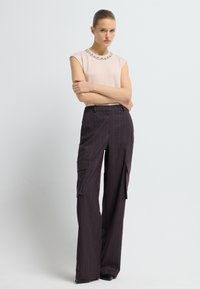 Top rosa claro de manga corta con cuello adornado con joyas, combinado con pantalones cargo de pierna ancha de rayas moradas oscuros que cuentan con bolsillos laterales.