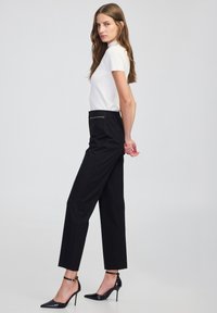 Witte T-shirt met korte mouwen gecombineerd met zwarte op maat gemaakte broek en zwarte pumps met spitse neuzen. De broek heeft een verzorgde uitstraling met een aansluitende taille.