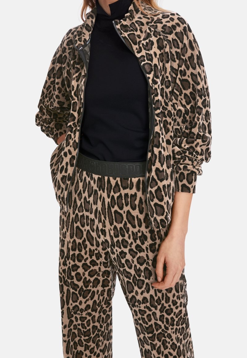 Dres w panterkę w odcieniu brązowym i czarnym. Miękki materiał, kurtka zapinana na zamek z bocznymi kieszeniami, pasujące spodnie z elastycznym pasem i detalem logo.