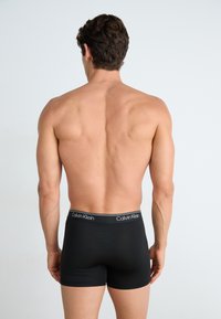 Zwarte aansluitende boxershorts met een zachte tailleband waar het witte "Calvin Klein" logo op staat. Gladde textuur, middelhoge pasvorm en een strakke snit.