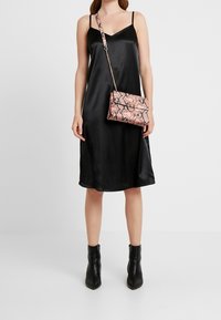 Abito slip in satin nero con spalline sottili, di lunghezza media. Abbinato a una borsa a tracolla con motivo pitone rosa e chiusura rotonda. Stivaletti neri alla caviglia.