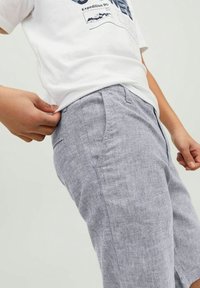 Harmaat pellavashortsit, joissa on sivutaskut, rento leikkaus ja teksturoitu pinta. Yhdistetty valkoisen graafisen T-paidan kanssa.