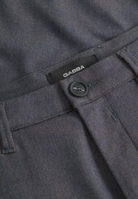 Pantaloni de culoare albastru închis, cu un model fin în carouri, dotati cu o închidere cu button, fermoar și o etichetă de marcă neagră "GABBA" pe talie.