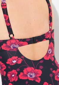 Maillot de bain une pièce avec un fond bleu marine orné de grands motifs floraux rouges et blancs, des bretelles réglables et un design de dos découpé.