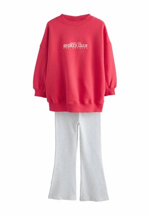 Rød oversized sweatshirt med teksten "SPORTS CLUB" kombineret med lysegrå vide bukser, vist på hvid baggrund.
