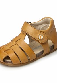 Ljusbrun lädersandal med utskuret mönster, justerbar rem och rund tå. Har ett vävt ovandel och en platt, texturerad sula.