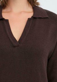 Brown knit sweater with a V-neckline and collar. The texture appears soft and slightly ribbed, showing subtle variations in thread thickness.