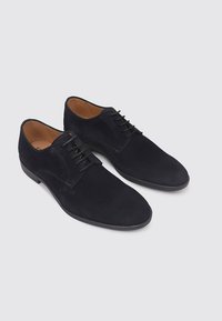 Chaussures en daim bleu marine avec une texture lisse, bout arrondi et design à lacets. Semelle en caoutchouc noir et détails de coutures minimalistes.