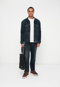 Traper jakna, tamnoplava, s dva džepa na prsima i srebrnim dugmadi; bijela majica ispod, tamne traperice, smešni tenisice i crna torba.