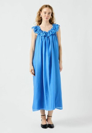 Blå maxi-klänning med volangkant i halsen, ärmlös design, flödande tyg och en mjuk textur. Bärs med svarta ballerina-skor.