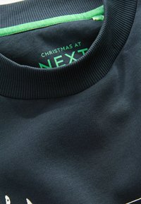 Felpa navy con colletto a costine e interno verde. Presenta il testo audace "Natale da NEXT" in verde brillante all'interno.