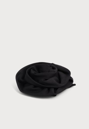 Tissu noir doux froissé en forme circulaire sur une surface blanche, montrant une texture lisse et des plis.