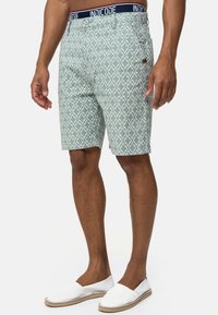 Shorts bleus clairs à motifs géométriques, dotés d'une taille bleu marine et d'une fermeture à bouton. Portés avec des espadrilles blanches.