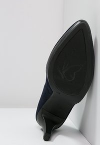 Scarpa con tacco alto di colore blu navy, con parte superiore in suede opaco e punta affusolata, suola in gomma nera con logo a farfalla e battistrada texture.