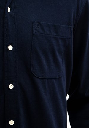 Marineblauw overhemd met knopen, gemaakt van een textiel met structuur. Voorzien van een borstzak en witte knopen aan de voorkant voor sluiting.