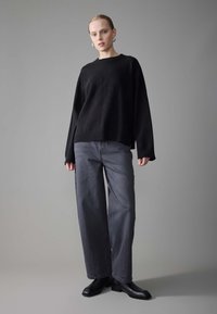 Black knit sweater with wide sleeves, paired with gray wide-leg jeans and black ankle boots. Simple, clean design with no visible patterns.