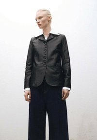 Crna kožna blazer jakna s zatvaranjem na osam dugmadi, šiljastim kragnom i dva prednja džepa. Nosi se preko tamnoplavih širokih traperica.